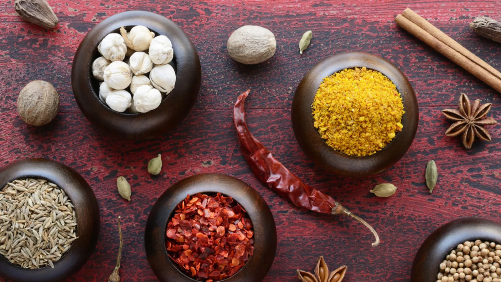 Whole spices being prepared in bowls on a red wooden table